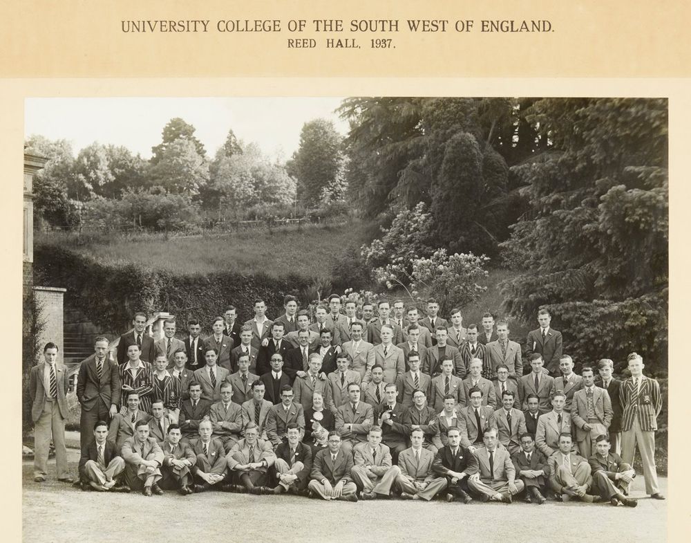 Formal black and white photograph mounted on card and entitled 'University College of the South West of England. Reed Hall. 1937.' Pictured are approximately eighty male students who lived in the hall of residence at Reed Hall. The front row is seated on the floor, the second row is seated on chairs, and the rows behind are standing. Also pictured are the matron, warden and president. The matron is holding a light-coloured adult cat on her lap and the president is holding a small black kitten with white socks.