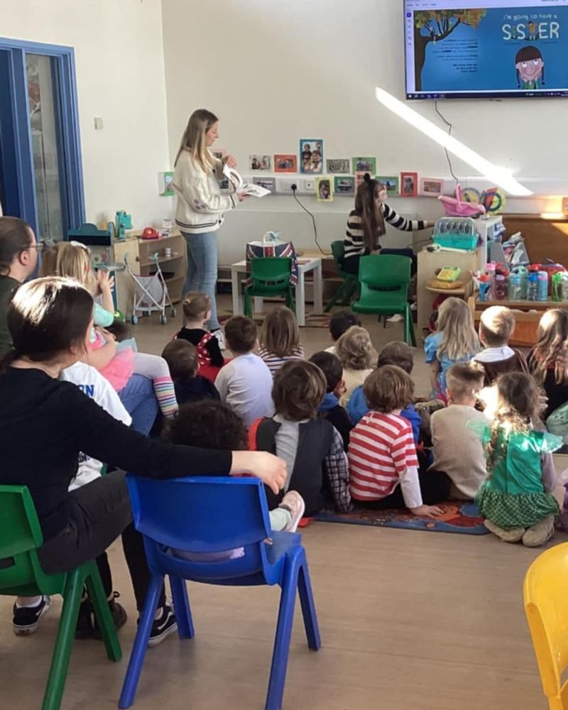 Photo of Laura Diebelius reading a book to a group of children in a classroom.
