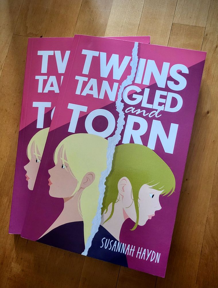 Photo of two copies of Twins Tangled and Torn on a wooden table.