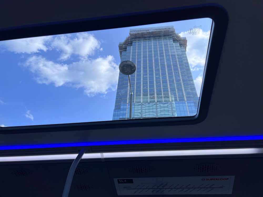 View through glazed roof of SL4 bus looking up at a tall building 