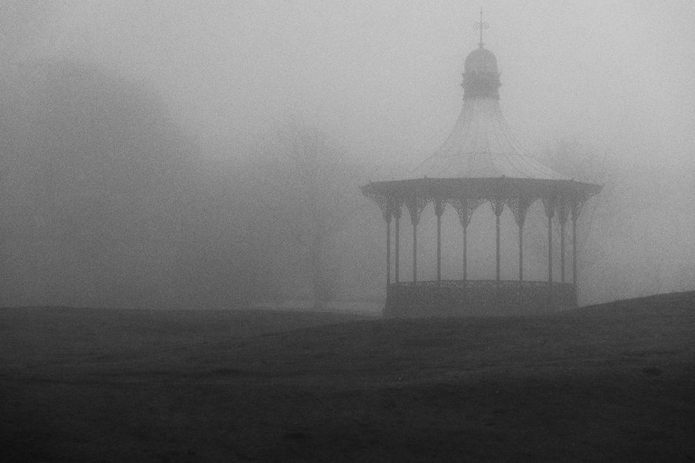 A gazebo bandstand, deep in the fog, edited to look like an old, eerie photo from the past or a horror movie.