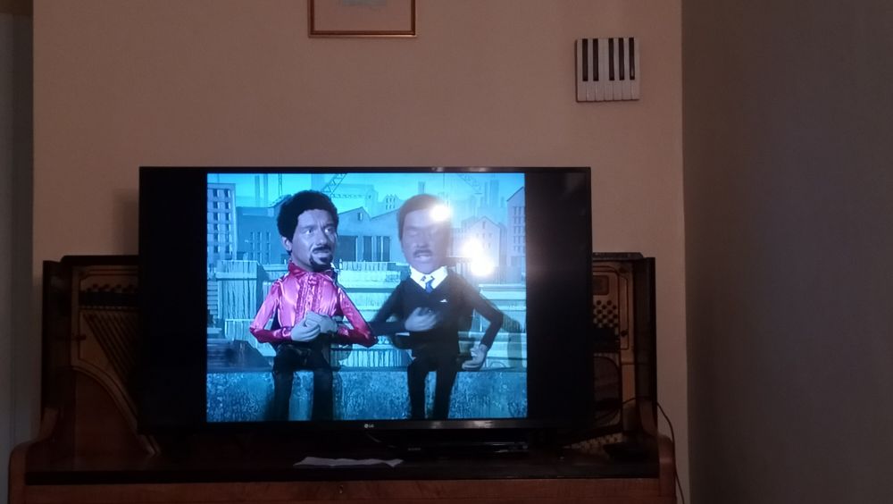 A TV on a broken piano. Otis Redding and Marvin Gaye are sitting on the dock of the bay. 