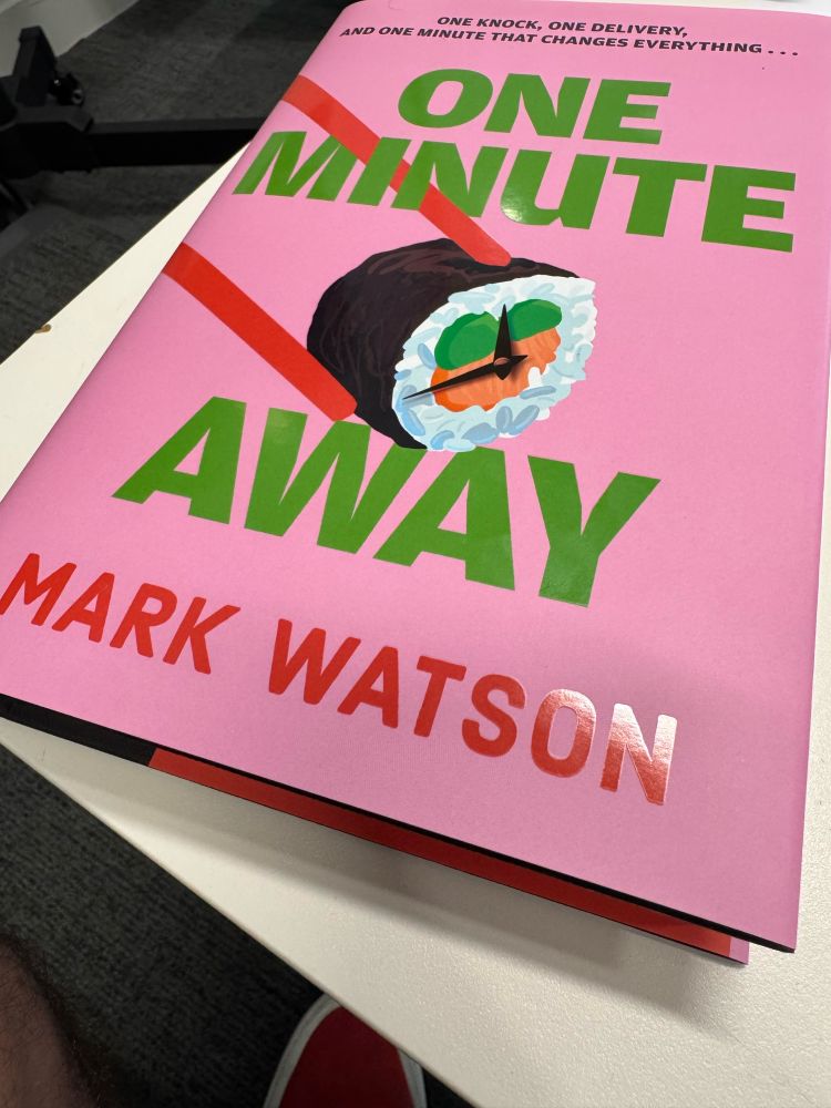 Pink book cover. One Minute Away in green type with Mark Watson’s name in red. Chopsticks hold a piece of sushi which appears to be a clock-face. It’s all shiny the way new books are.