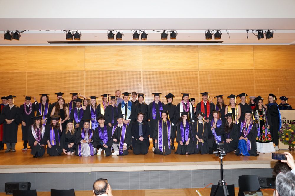 Class of 2025 standing on stage in cap and gown with ESS Faculty.