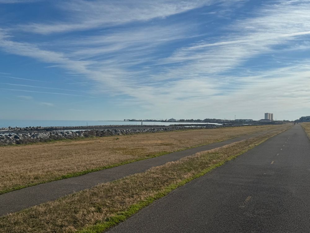 Bucktown Marina pictured with running path, marsh, water, and slightly cloudy morning sky. 