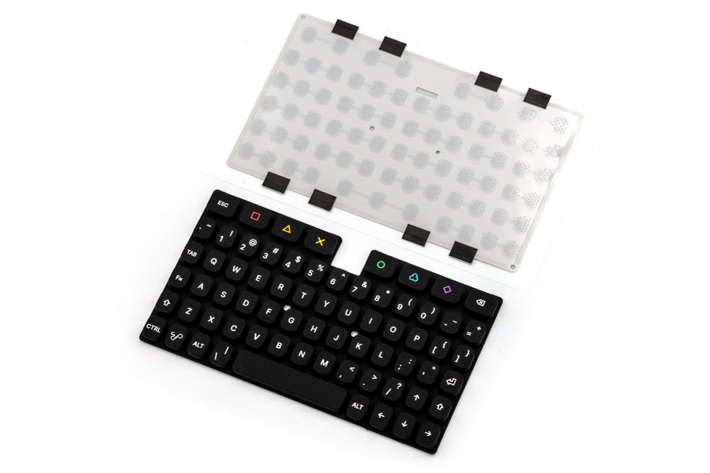 A photo of the KeebDeck Keyboard keypad and dome sheet. The dome sheet has many domes visible through the white plastic, and 8 black pieces of tape to cover where the backlight LEDs would be. The Keyboard has 69 keys with the usual PC layout, and a few extra ones color symbols and colors.