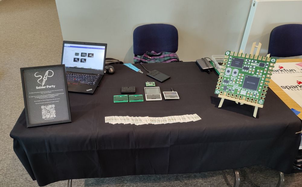 A table with the Solder Party standee, the 10x Stamp, stickers, and lots of keyboard PCBs. 