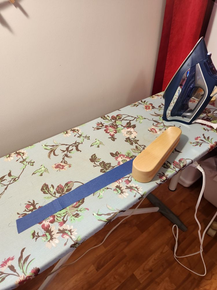 A strip of fabric on an ironing board, with a clapper on it to set the fold.