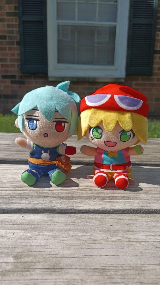 Sig (left) and Amitie (right) plushies sitting next to each other on a wooden bench. 