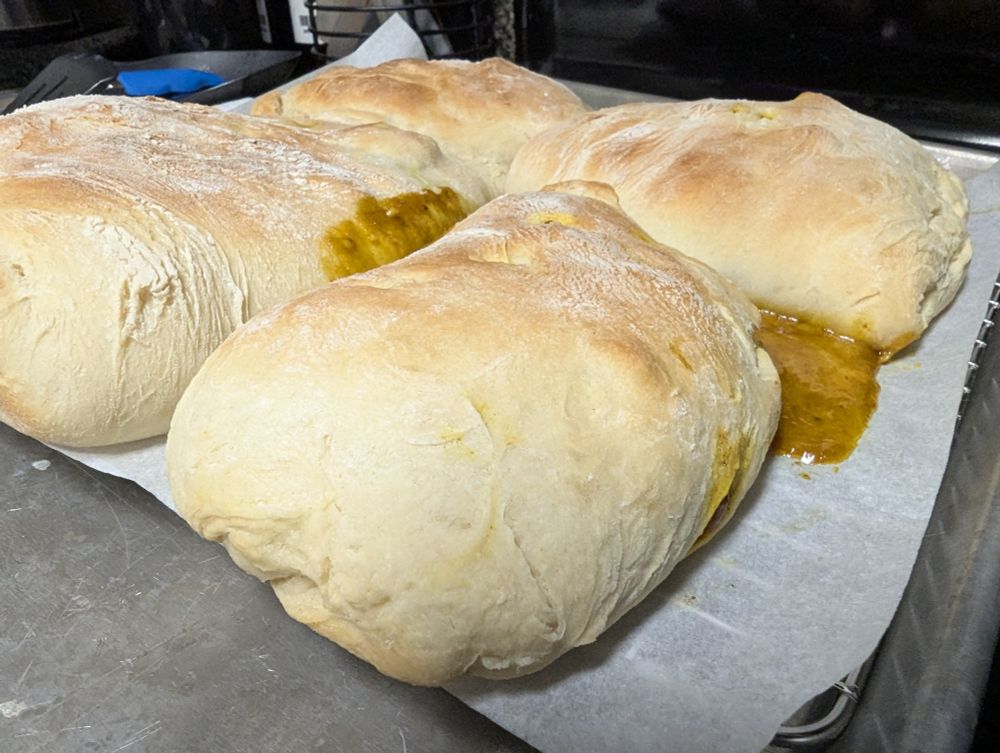 four calzones leaking brown sauce, tightly grouped on a cooling rack, from an inscrutable angle that betrays any training in photography the cook may have had