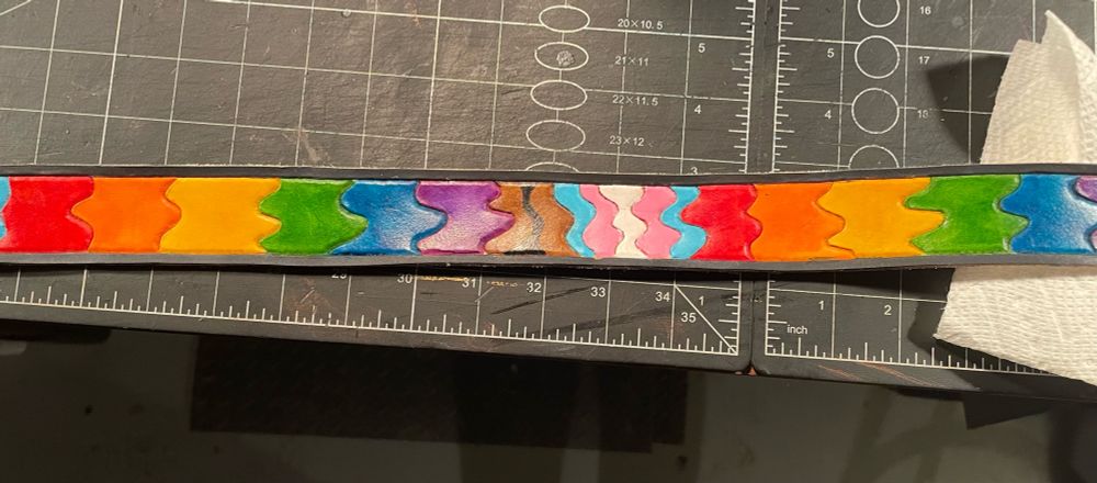 Pictures is a section of belt, painted with the colours of the trans flag in between two rainbows. The lines defining each colour are random squiggles. 