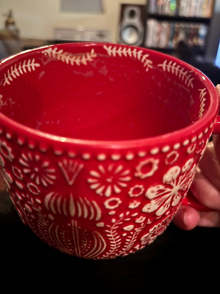 Mug with residue of hot chocolate, sitting atop a black cat, sitting on my lap. 