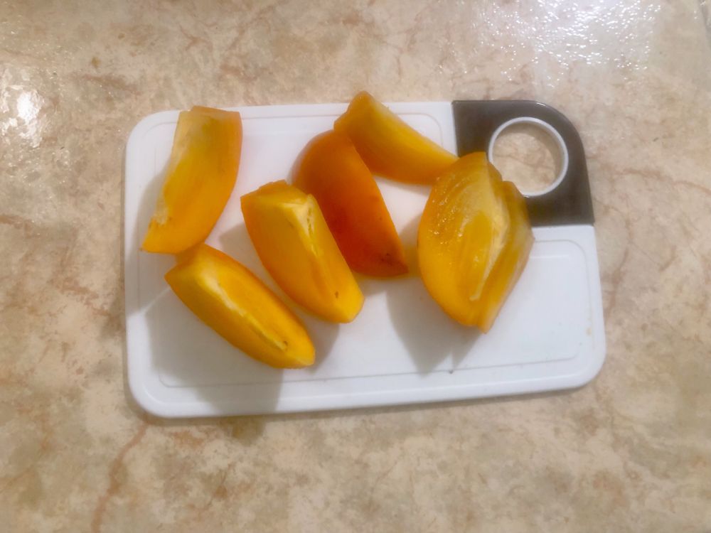 A white cutting board with a cut up juicy looking persimmon on it 