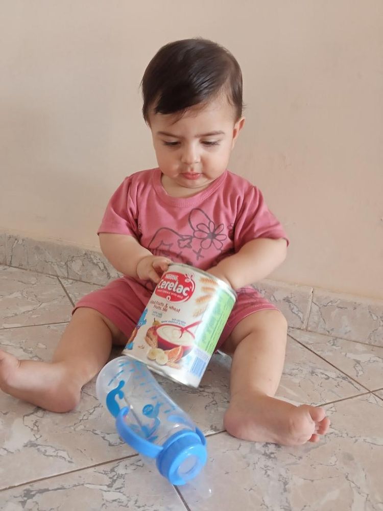 A baby sitting on the floor with an empty can of formula 