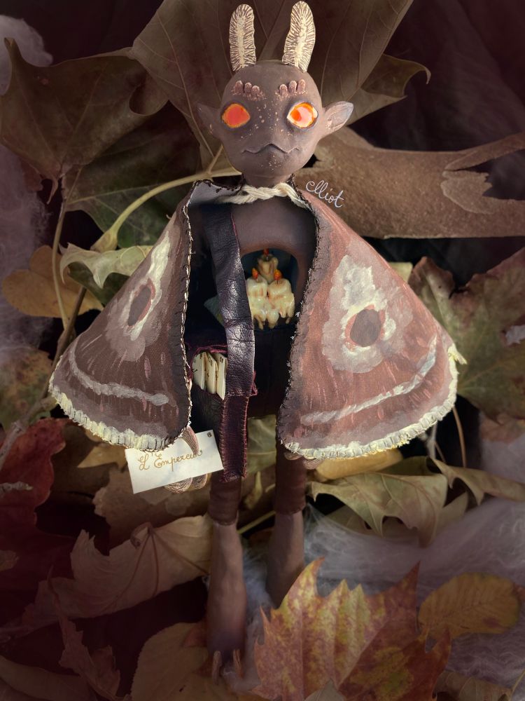 Picture of a moth character with candles in its chest. It had antennaes and wings, holding a letter in its claws. The background is leaves.