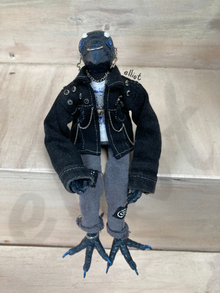 Picture of a sitting doll, a punk magpie with a jeans jacket and blue fingernails