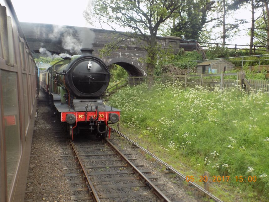 Dark green steam locomotive travelling along the adjacent track to the train I photographed it from, passing under a bridge in the process