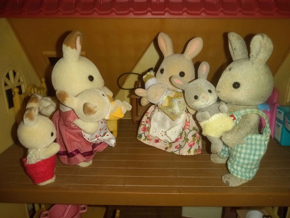 A set-up of Sylvanian Families figurines. Chocolate Rabbit baby Crème Chocolate is looking at three rabbit parents holding their respective babies.