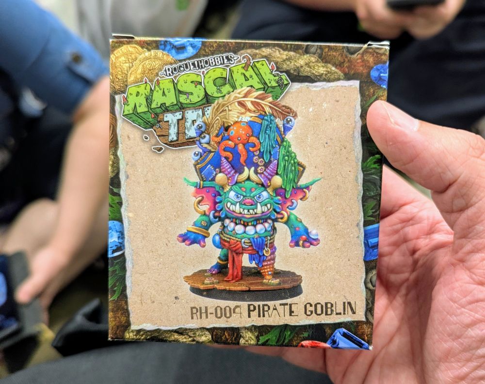 A hand holding a colorful box for a Rogue Hobbies Rascal Town pirate goblin miniature.