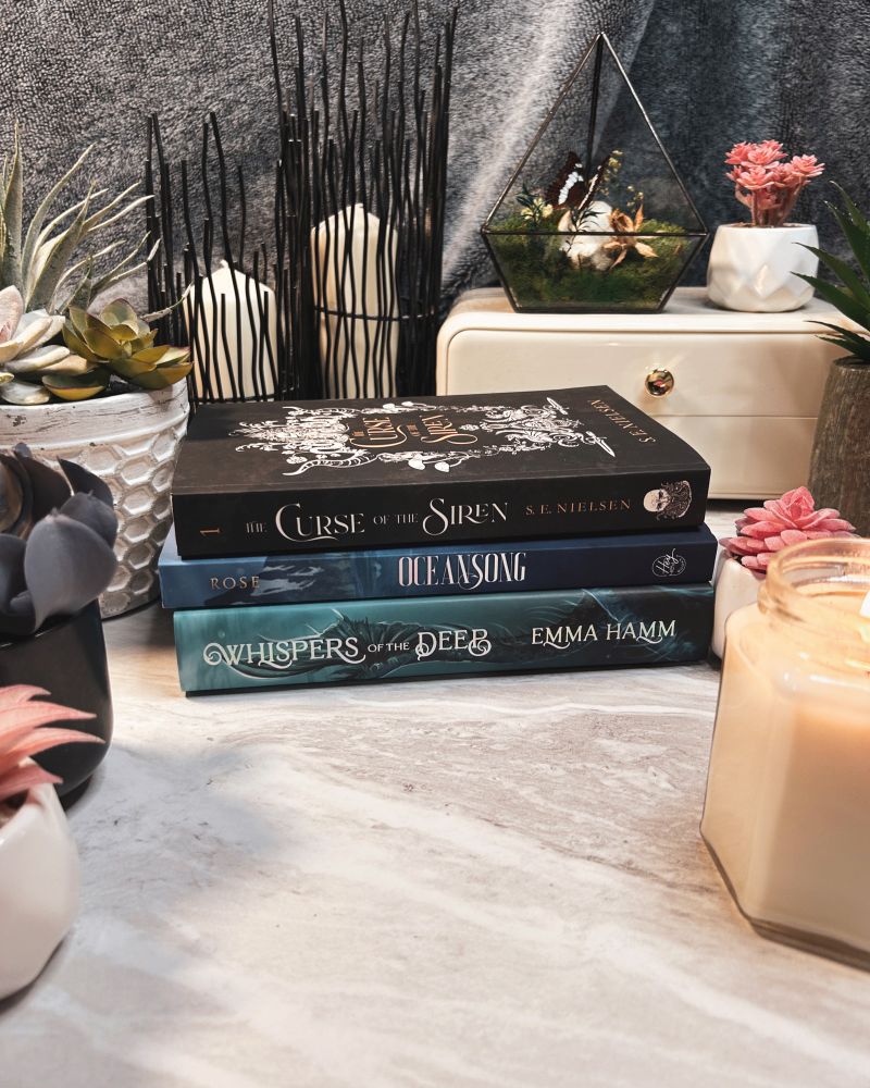 Book stack of The Curse of the Siren by S.E. Nielsen, Oceansong by C.W. Rose and Whispers of the Deep by Emma Hamm