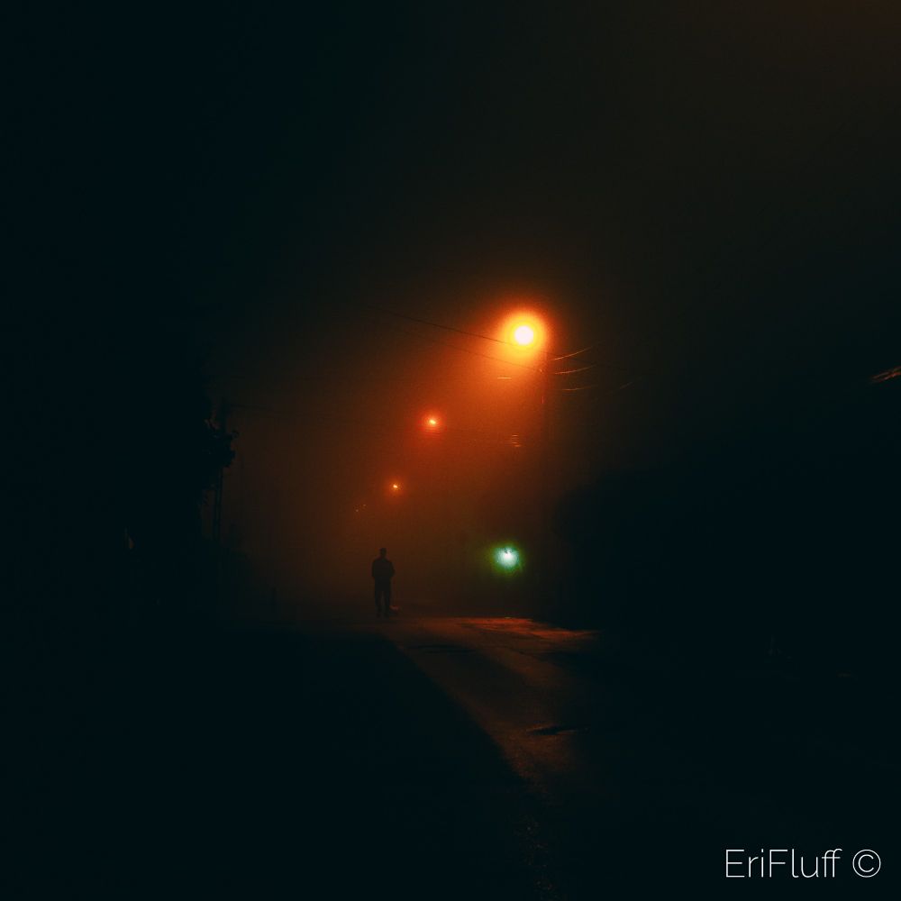 A shadow man standing in the middle of a misty street at night