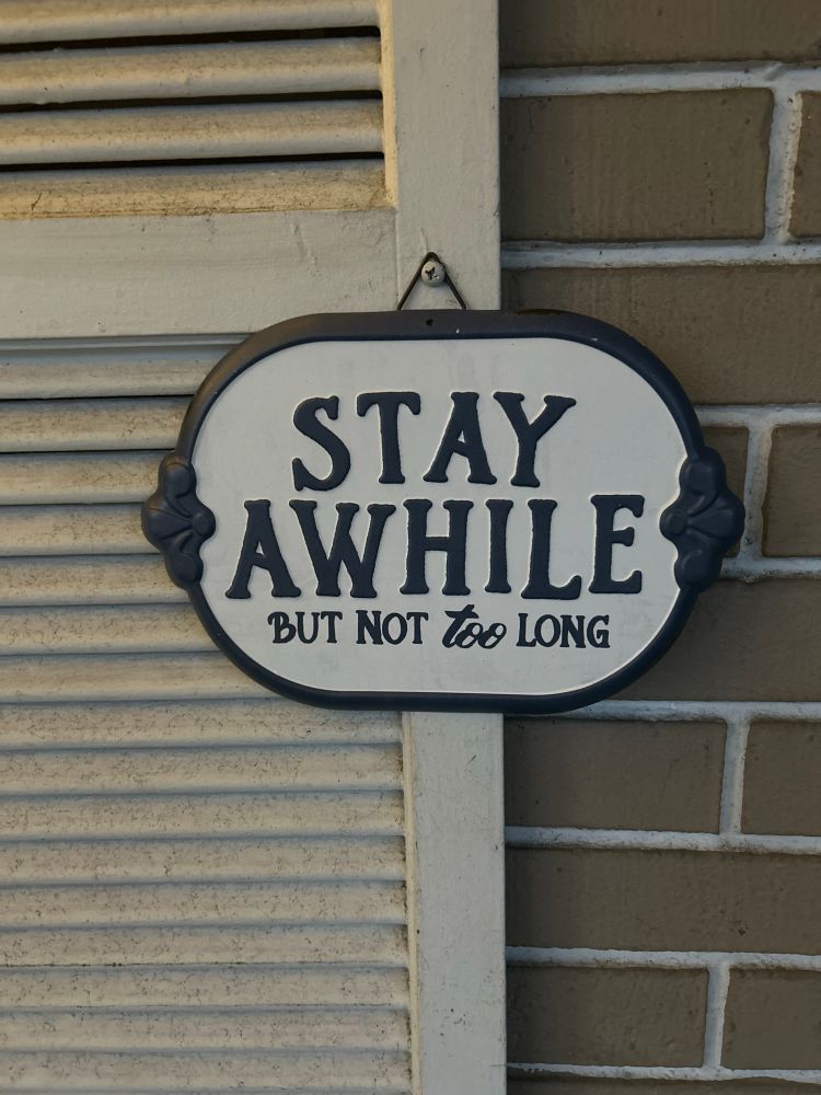 Sign hanging on a shutter says Stay awhile but not too long 