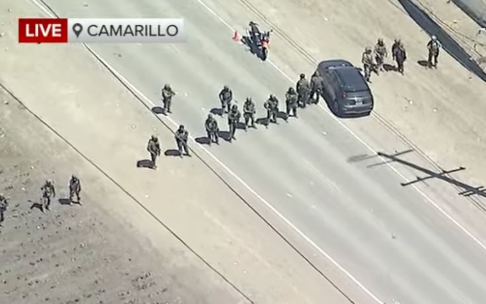 A bunch of the dipshit thugs standing in a line across a road, with a car sorta haphazardly parked on one side