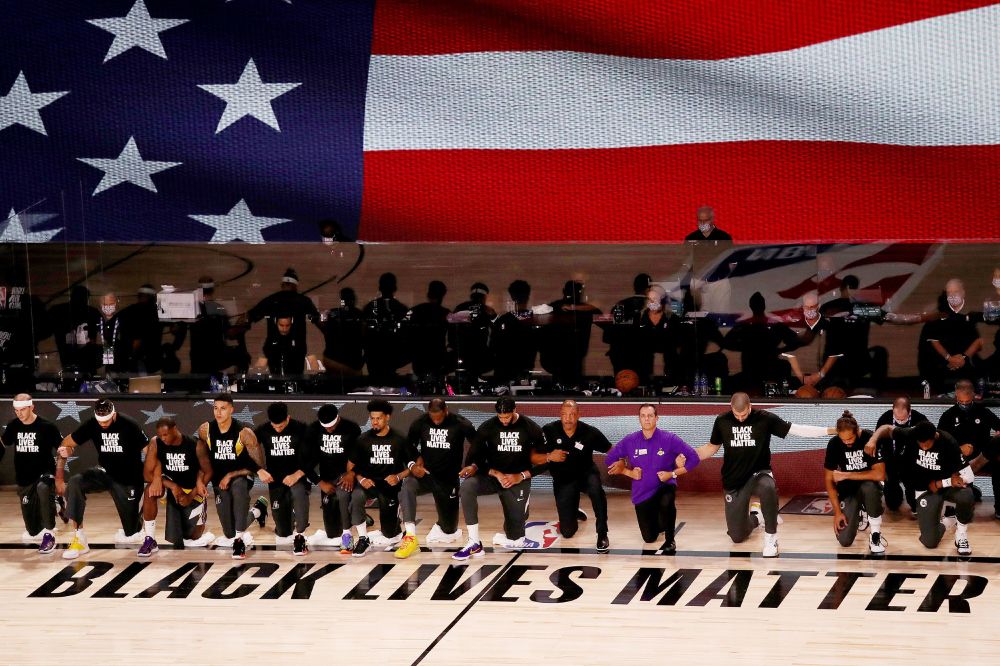 "Black Lives Matter" printed on an NBA basketball court, with players and others kneeling and wearing "Black Lives Matter" shirts