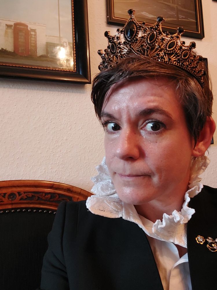die gleiche Person aus dem vorigen Bild sitzt auf einem Biedermeier Sofa und trägt eine Modeschmuckkrone mit schwarzen Steinen