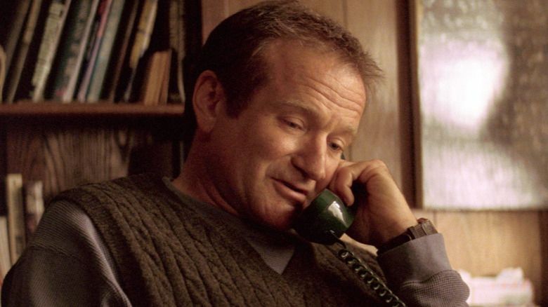 robin williams in Insomnia on the phone, looking vaguely amused. he has a brown knit sweater vest in a dark wood paneled study