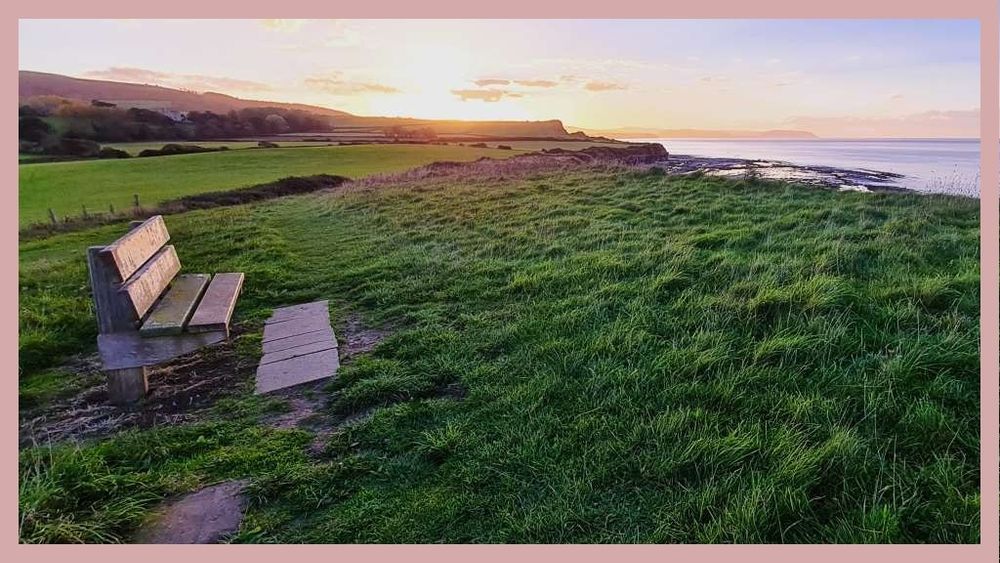 a wooden bench on a grassy hilltop looking out to sea as the sun sets over the cliffs in the distance. No one else around. It was October and a slight chill in the air but wonderful to sit here and enjoy the air and the sounds and the sense of place. 
