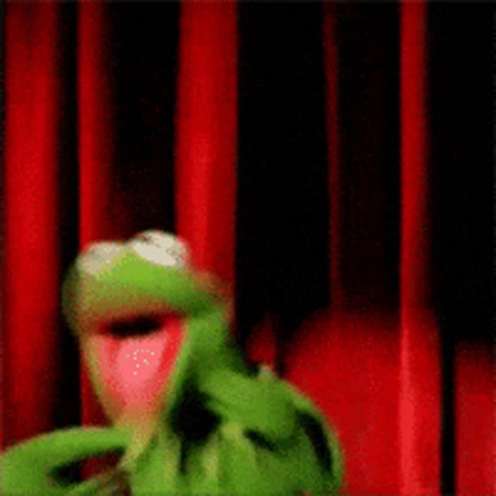 kermit the frog is standing behind a red curtain .