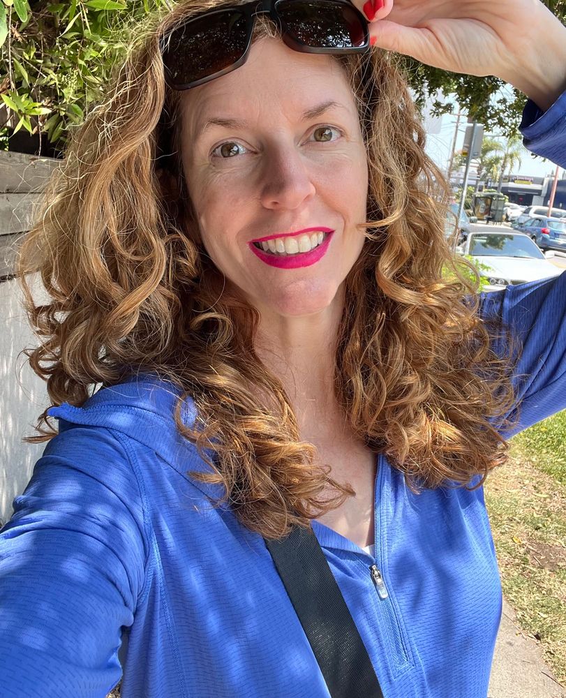 Jendia Gammon in LA in a blue hoodie, lifting up sunglasses on the top of her head

