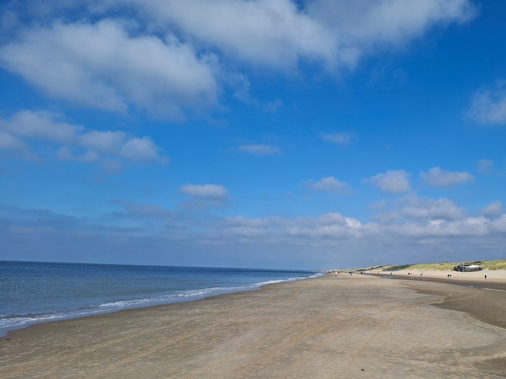 Strand mit Meer und Dünen im Hintergrund. 