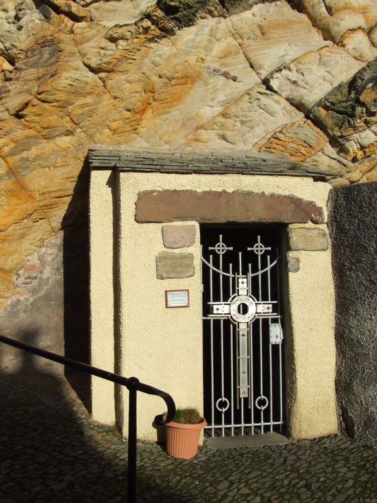 A photo of an iron gate with a cross on it set in a stone wall. It's the entrance to St Fillan's Cave.