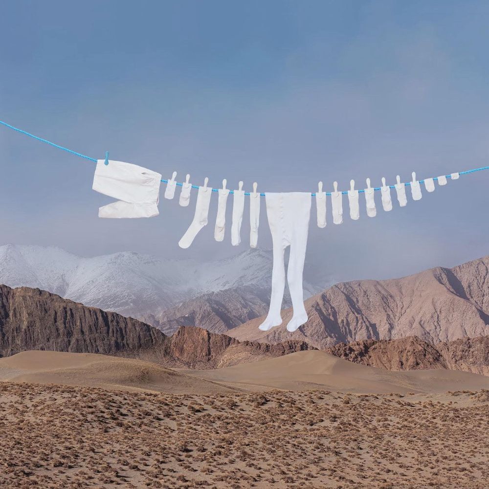 Laundry line with white clothing articles hung in a shape of a dinosaur with a desert mountain background 