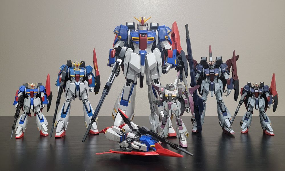 Various gunpla models of MSZ-006 Zeta Gundam. They are standing on a black table with a white wall in the background. From left to right:
-HGUC 1/144 MSZ-006 Zeta Gundam (U.C. 0088) (unpainted)
-MG 1/100 MSZ-006 Zeta Gundam Ver.Ka (unpainted)
-PG 1/60 MSZ-006 Zeta Gundam (unpainted)
-HGUC 1/144 MSZ-006 Zeta Gundam (painted in Zeta Gundam 3A colors)
-MG 1/100 MSZ-006 Zeta Gundam Ver.2.0 (painted in standard colors)
-HGUC 1/144 MSZ-006 Zeta Gundam (G.E.P.) (painted in standard colors)

WAVERIDER MODE (front row):
-RG 1/144 MSZ-006 Zeta Gundam (unpainted)
