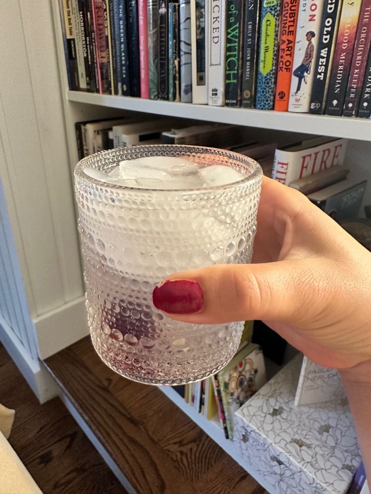 Cara’s hand holding up a glass to the camera as a toast.