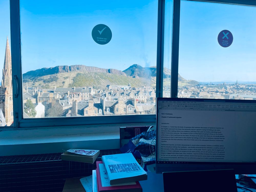 A photo of my office. In the background, out of the window, you can see Arthur’s Seat and the Salisbury Crags, while in the foreground there’s my desk with a large computer monitor and a stack of books with one called “Philosophical Methodology’ on top.