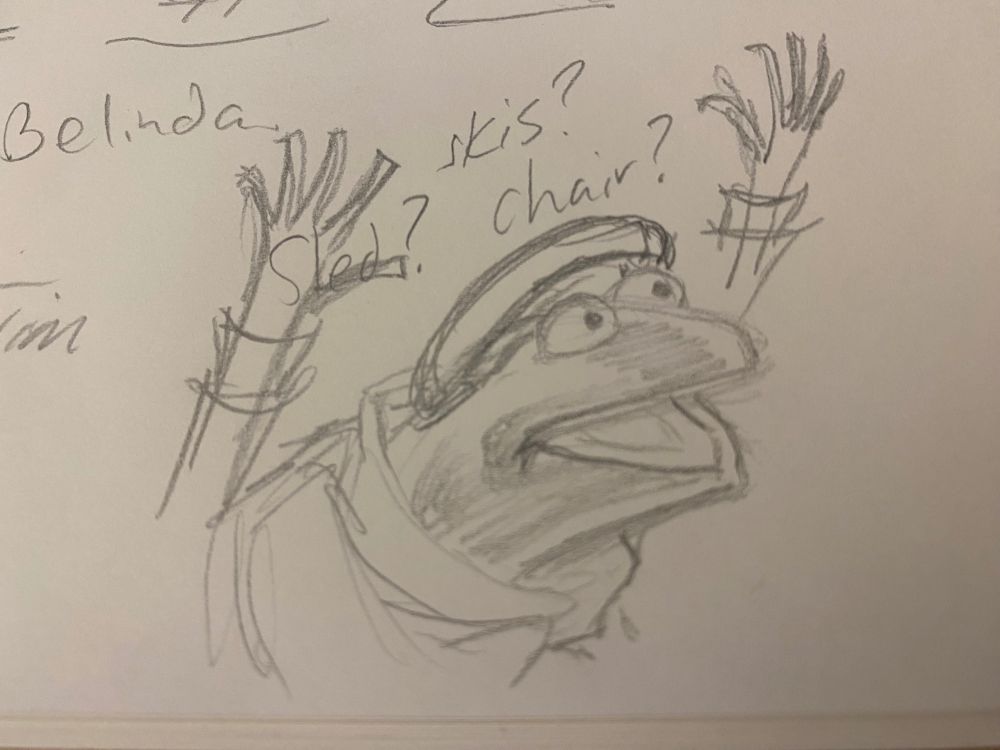 A pencil sketch of Robin from the Muppets, as Tiny Tim from a Muppet Christmas Carol. His mouth is open and his arms are both up in the air. Sled? Skis? Chair? Belinda Tim are words quickly written around the drawing. 