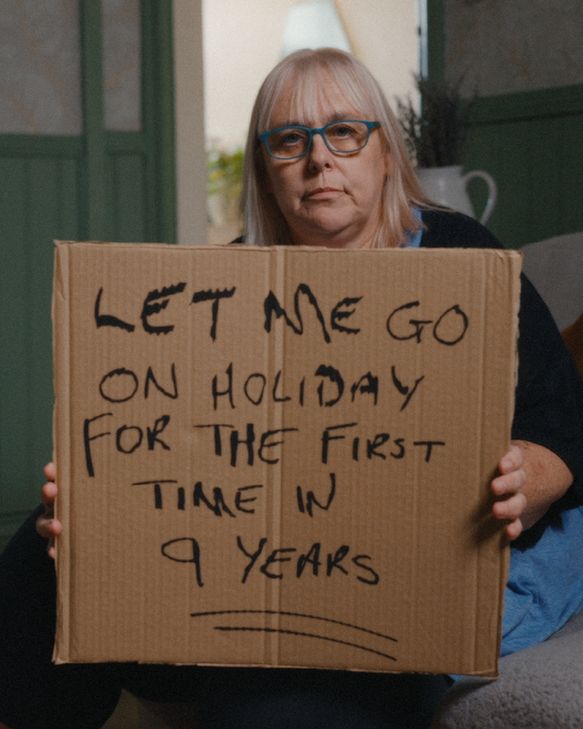 A picture of a carer holding up a cardboard sign that says 'Let me go on holiday for the first time in 9 years'