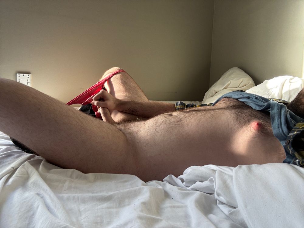 A guy in bed with his pants and visible thong pulled down 
