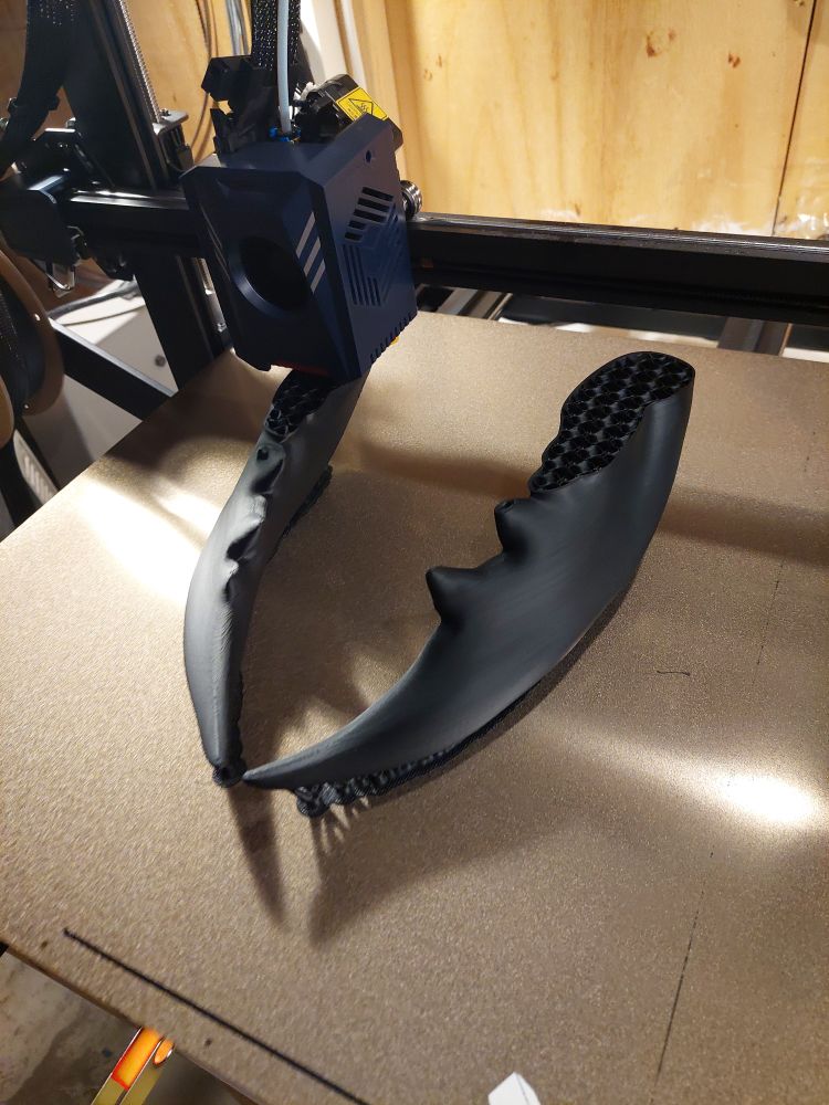 A 3d printer in the process of printing a pair of large beetle-esque mandibles in black plastic.