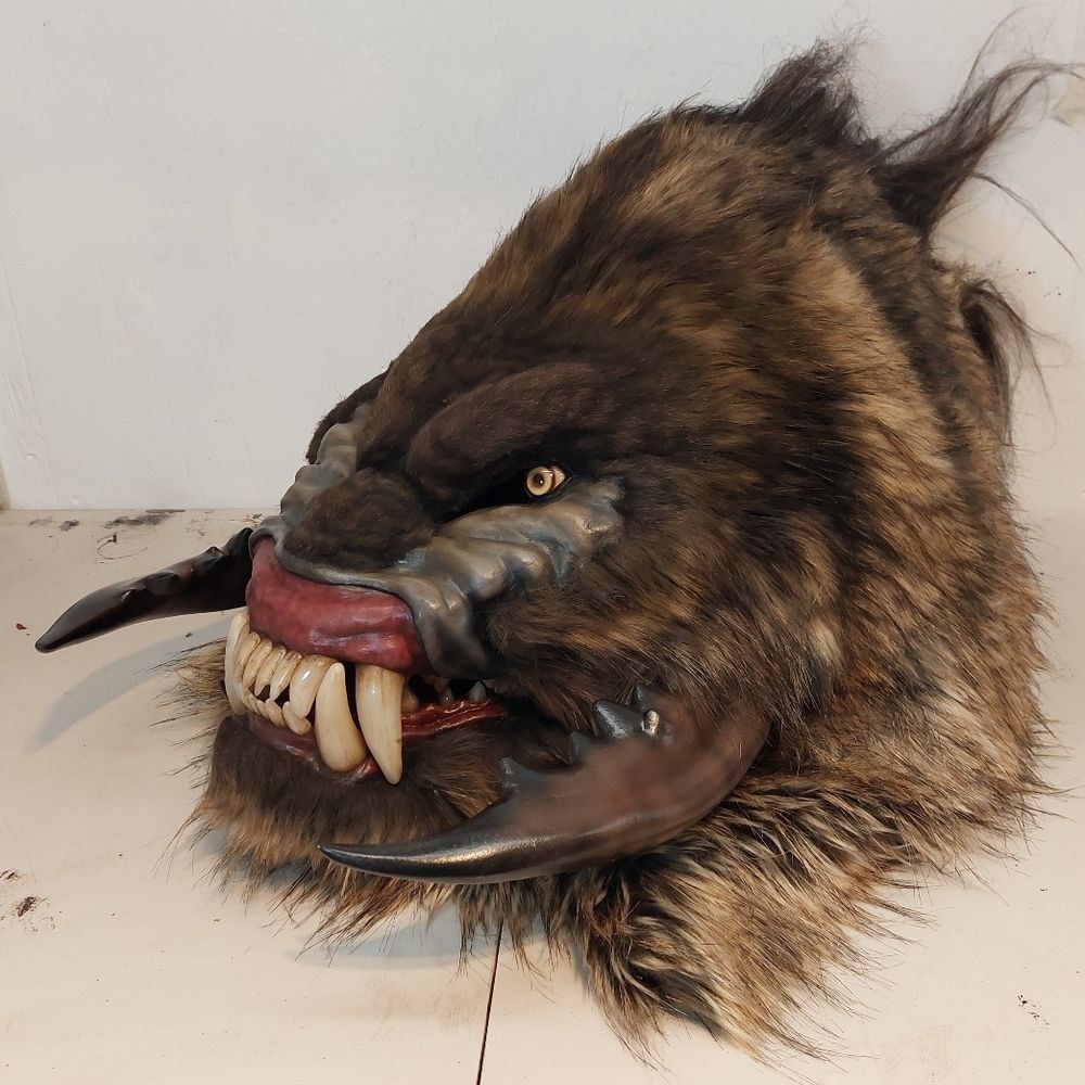 A brown-furred monster head with a mandrill-like snarl, intense yellow eyes, and crab-claw-like facial extensions. 3/4 view.