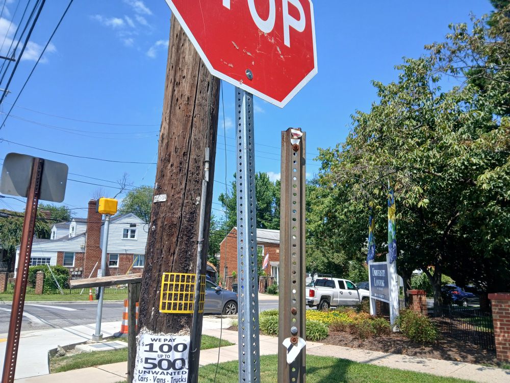 Just outside Takoma Park, Maryland, view west along north side of University Boulevard east of Merrimac Drive. In foreground, an empty metal sign pole to the right of a wooden utility pole and top sign.
