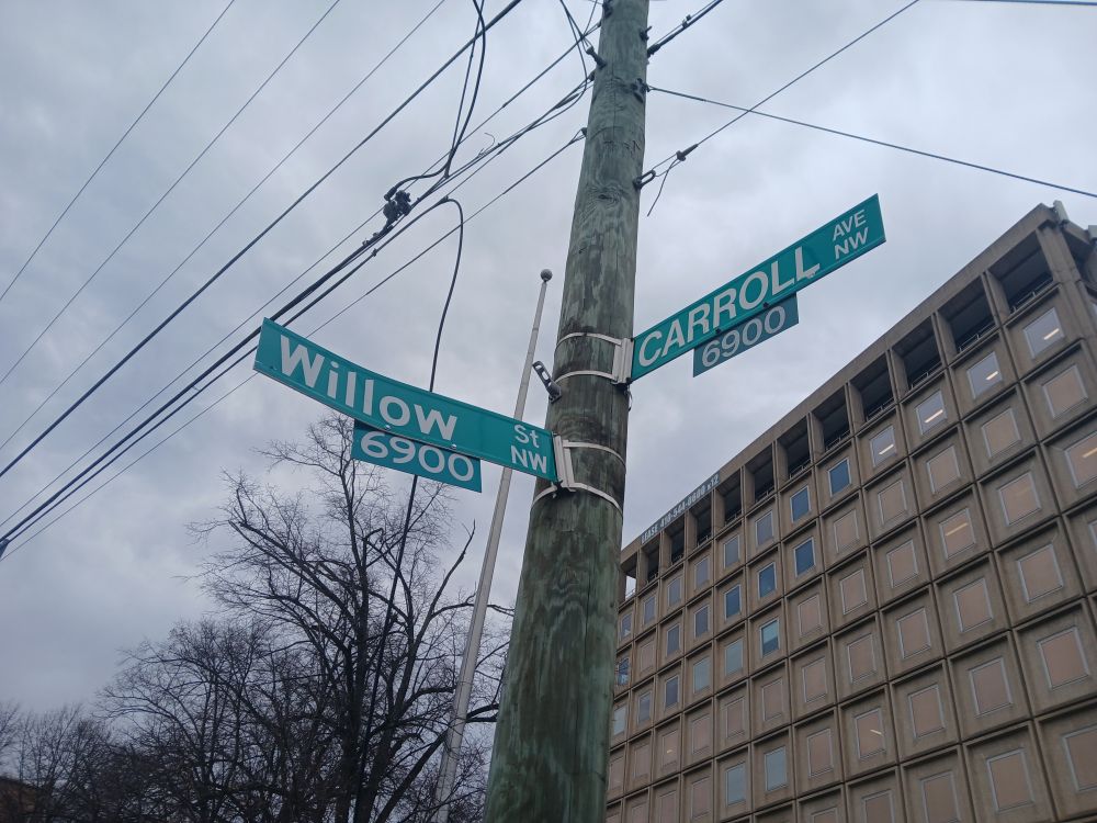 Closeup of white-on green street name signs, one with the text "CARROLL AVE NW 6900."
