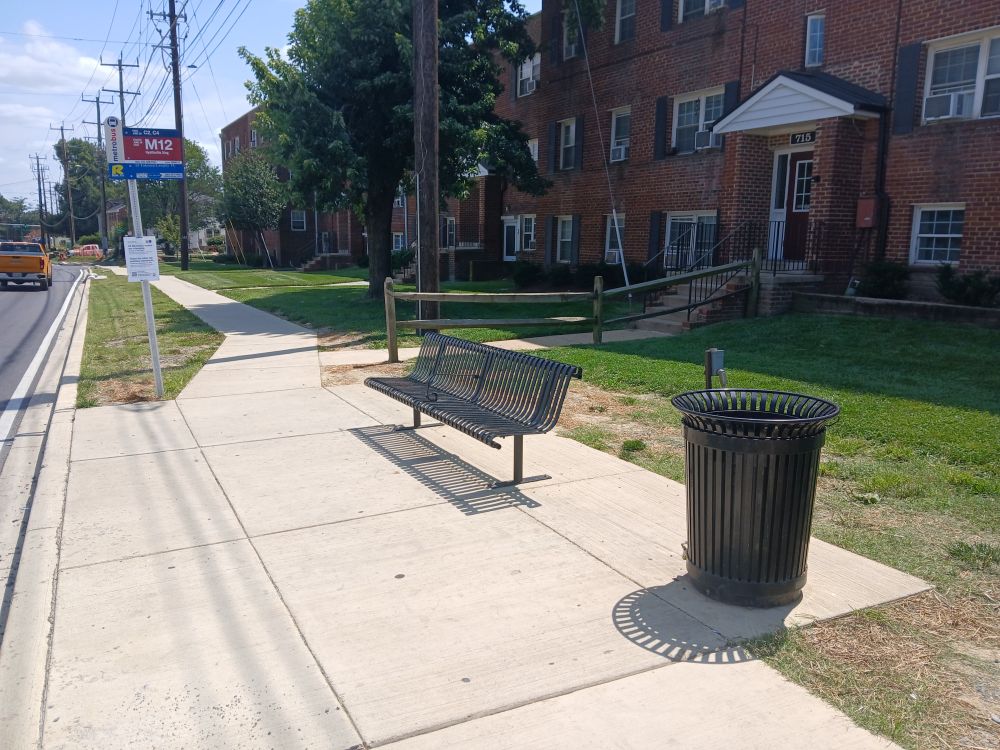 In Silver Spring, Maryland, southeast corner of intersection of University Boulevard and Piney Branch Road. Bus stop signs are visible, as is a bench and trash receptacle; no shelter is visible.