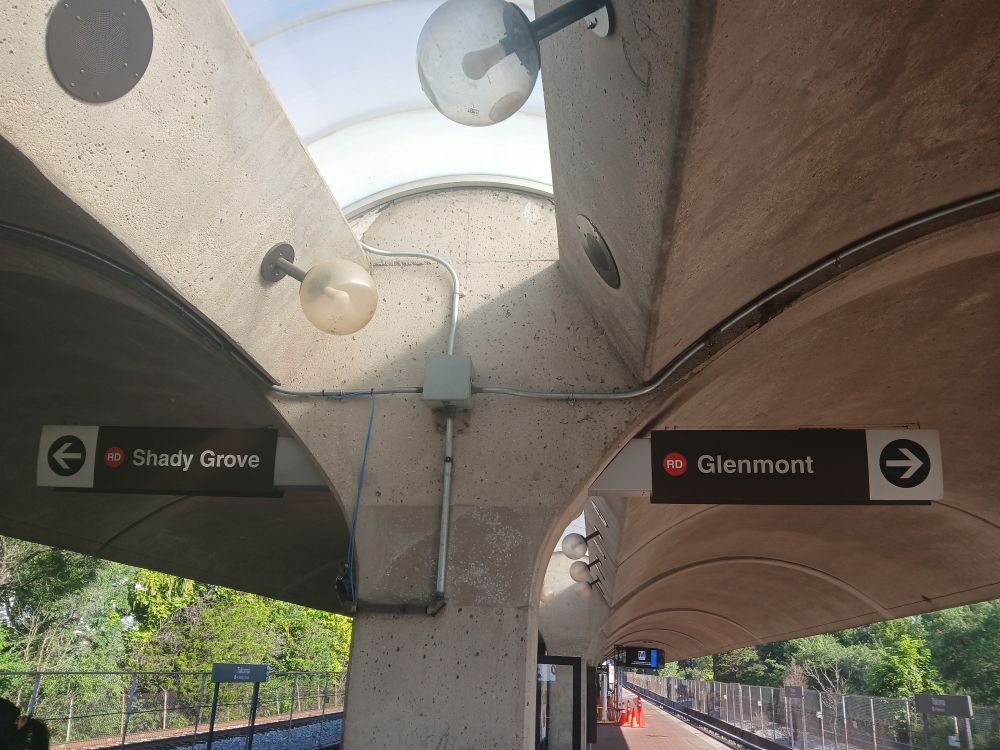 On an outdoor rail platform, overhead white-on-brown signs with the destinations Shady Grove and Glenmont.