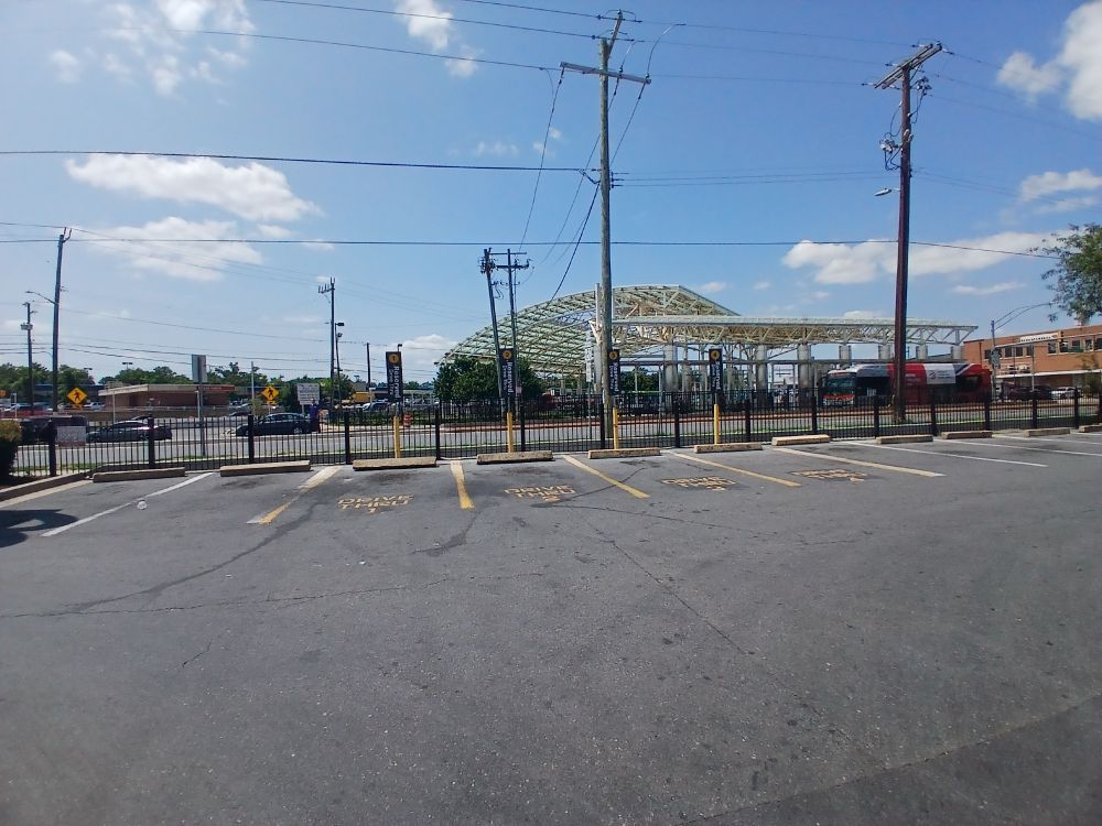 Just outside Takoma Park, Maryland, a McDonald's parking lot with spaces labeled "DRIVE THRU 1" through "DRIVE THRU 4." There are vertical signs at the head of each space. In background, across New Hampshire Avenue, the Crossroads Transit Center.