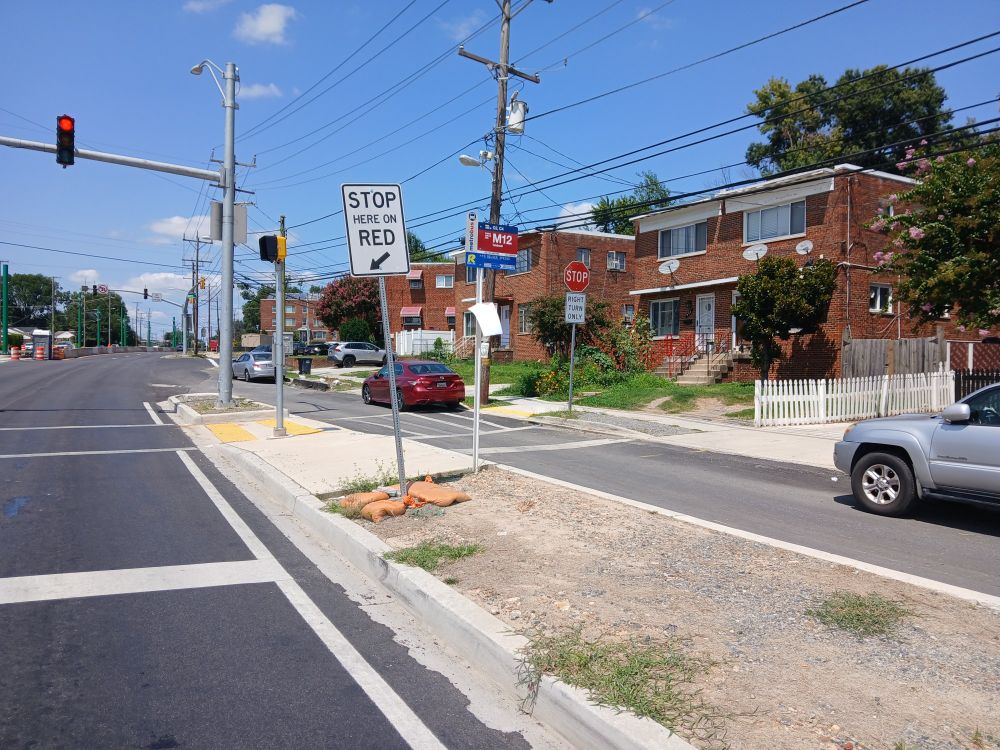 Just outside Takoma Park, Maryland, view west along north side of University Boulevard east of Carroll Avenue. Bus stop signs are visible; no shelter, seating, or receptacles are visible.